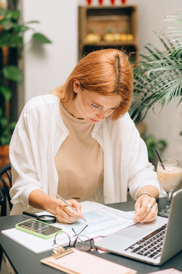 why-choose-us Woman analyzing financial documents using laptop and calculator indoors.